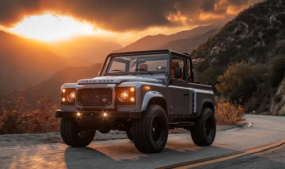 Defender restauré haut de gamme, intérieur cuir visible, sur une route de montagne
