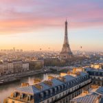 Vue panoramique de Paris au lever du soleil avec la Tour Eiffel au centre sous un ciel rose et orangé.